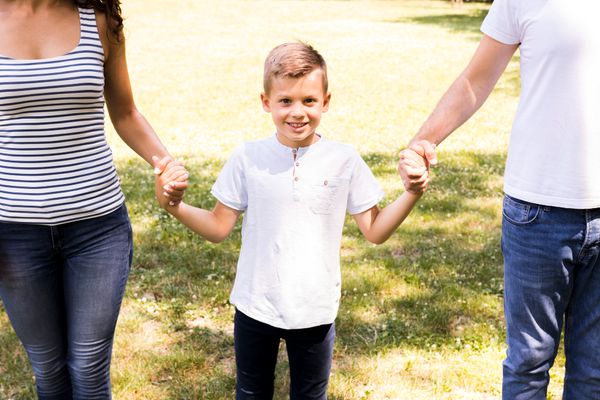 ילד מאושר עומד ומחזיק בידיים של ההורים שלו כאשר הם משני צדדיו